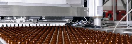 Rzędy wyprodukowanych maszynowo czekoladek na przenośniku w fabryce czekolady
