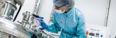 Arbeiter in einem Pharmaunternehmen liest eine Anzeige an einem Reaktor zur Herstellung von Arzneimitteln ab.